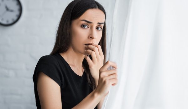 scared young woman looking at camera while standing by window and suffering from panic attack
